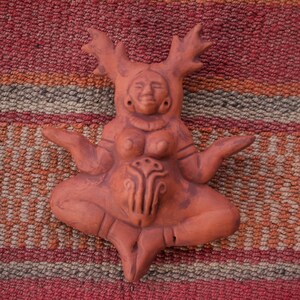 Op de afbeelding: Een terracotta beeld van een vrouwelijke figuur met geweien, zittend in een meditatieve houding. De figuur heeft een gedetailleerd gezicht en een bloemmotief op de buik.