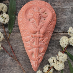 Op de afbeelding: Een terracotta wierookbrander in de vorm van een hart met een gedetailleerd ontwerp van een slang, een zon en een gestileerde menselijke figuur. De brander heeft meerdere gaten voor wierookstokjes.