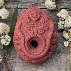Op de afbeelding: Terracotta wierookbrander met een gedetailleerd ontwerp van een vrouw met een vlinder en een slang. De brander heeft een gat in het midden om wierook te branden.