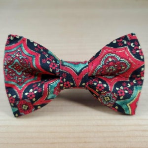 May include: A red, green, and gold patterned bow tie. The bow tie has a geometric design with a black background.