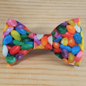 May include: A colorful bow tie with a pattern of jelly beans. The bow tie is made of fabric and has a bright, cheerful design.