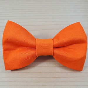 May include: A bright orange bow tie made of fabric. The bow tie is tied and ready to wear.