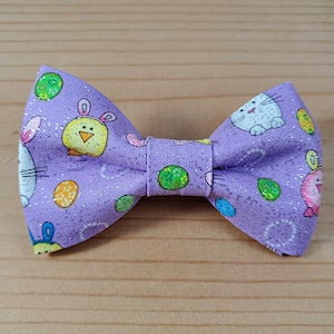 May include: Purple bow tie with a glittery finish and a repeating pattern of Easter eggs, chicks, and bunnies.