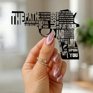 May include: A black cutout in the shape of a handgun featuring the text of the Ezekiel 25:17 passage from the movie Pulp Fiction. The text is arranged to form the silhouette of the firearm and includes a small graphic of a man in a suit.