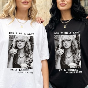 May include: Two t-shirts, one white and one black, each featuring a black and white image of Stevie Nicks. The text "DON'T BE A LADY" is above the image, and "BE A LEGEND -STEVIE NICKS" is below.