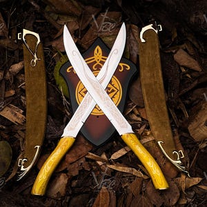 May include: Two crossed fantasy swords with ornate white blades and yellow handles, set against a backdrop of brown leaves. The swords are in front of a shield with a gold and black design, and are flanked by two brown sheaths with gold detailing.
