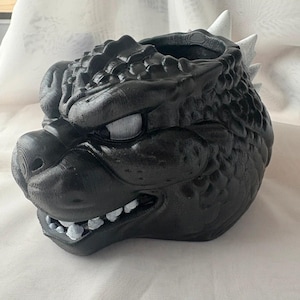 Peut inclure: Pot de tête de dragon noir avec des détails blancs sur les dents et les pointes. Le pot a une surface texturée et une large ouverture pour les plantes. Le visage du dragon est détaillé avec des écailles et une expression féroce.