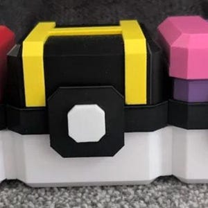 Puede incluir: Tres contenedores rectangulares con forma de esferas estilizadas, cada uno con base blanca, banda central negra con un octágono blanco y una parte superior distintiva. El primero es rojo, el segundo negro con detalles amarillos y el tercero rosa y morado con una M.