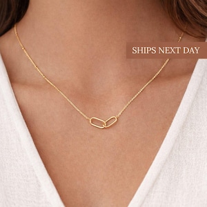 May include: A fine gold necklace with two linked oval pendants. The necklace hangs from a delicate chain. The image includes the text "SHIPS NEXT DAY". The necklace is displayed on a person's chest.