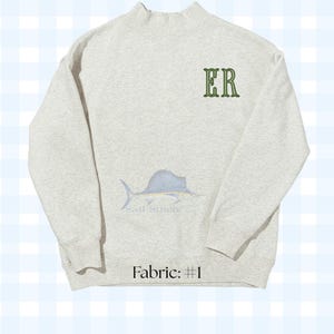 May include: A light gray heathered mock neck sweatshirt featuring the embroidered green letters ER on the upper left chest. A light blue sailfish illustration is centered below the letters with the text Sail Stitch and Fabric: #1 below.