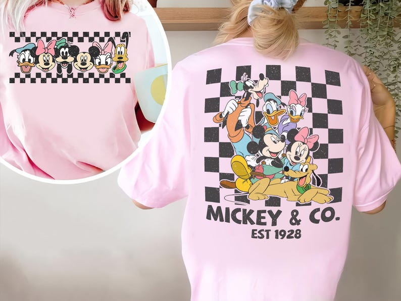May include: A light pink t-shirt featuring a large graphic on the back of Mickey Mouse, Minnie Mouse, Donald Duck, Daisy Duck, Goofy, and Pluto over a black and white checkered square. The text MICKEY & CO. EST 1928 is printed below the graphic.