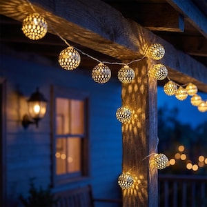 Puede incluir: Cadena de luces decorativas con globos que emiten un brillo cálido. Los globos metálicos tienen un diseño calado, creando intrincados patrones de luz. Las luces están ensartadas en un cable blanco, ideal para la decoración exterior.