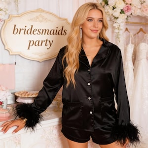 May include: Black satin pyjama set with feather trim on the cuffs. The set includes a button-down shirt and shorts. The image also features a sign that says "bridesmaids party".
