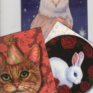 May include: A collection of illustrated cards featuring animal portraits. Includes a barn owl against a starry blue background, a cat wearing a party hat, and a white rabbit surrounded by red roses.