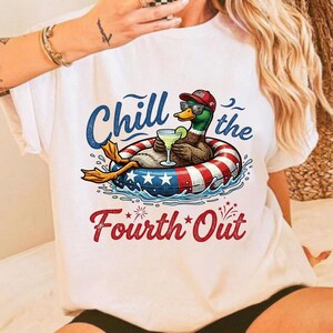 Könnte beinhalten: Weißes T-Shirt mit einer Grafik einer Ente in einem rot-weiß-blauen Schwimmring, die eine Sonnenbrille und eine Mütze trägt und einen Cocktail hält. Der Text lautet "Chill the Fourth Out" in Blau und Rot.