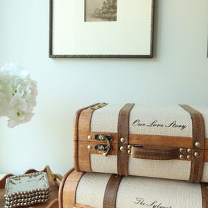 Custom memory trunk set with vintage suitcase styling, including cream canvas keepsake boxes with wood trim and leather accents. Elegant wedding keepsake storage for bridal shower gifts, couples’ memory boxes, engagement decor, and sentimental photo storage.