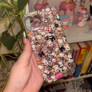 May include: A clear phone case adorned with multiple Hello Kitty figures, rhinestones, and heart-shaped embellishments. The case incorporates a leopard print pattern and the text "I ❤️ ME".