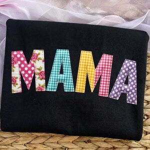 Puede incluir: Bolso tote negro con la palabra "MAMA" aplicada en tela estampada colorida. Las letras son de lunares rosas, floral, cuadros vichy turquesa, cuadros vichy amarillos, cuadros vichy rosas y lunares morados.