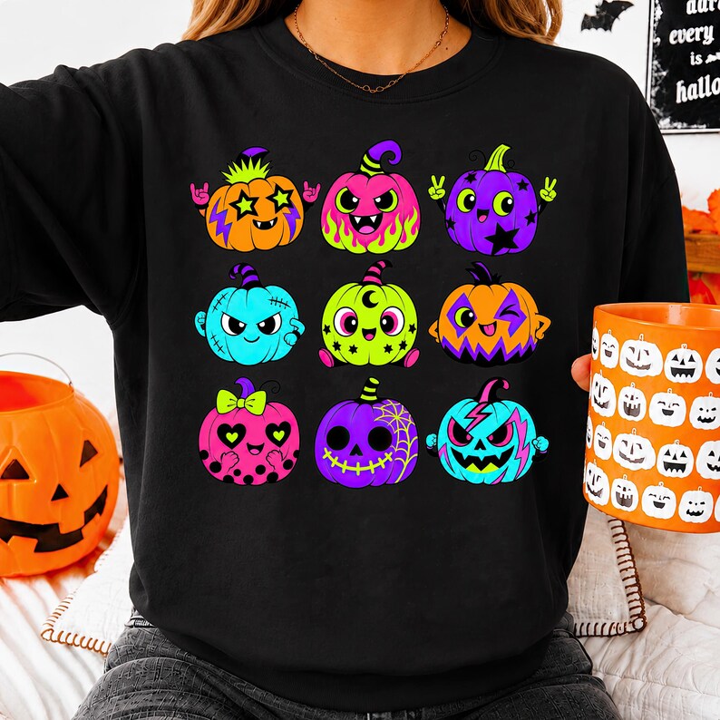 Puede incluir: Una sudadera negra de cuello redondo con un estampado gr&aacute;fico de nueve calabazas de dibujos animados coloridas. Cada calabaza muestra una expresi&oacute;n &uacute;nica y una paleta de colores vibrantes, incluyendo tonos naranja, rosa, morado, verde lima y azul brillante.