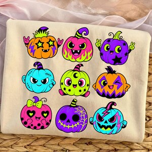 Puede incluir: Una sudadera de color crema con un estampado gr&aacute;fico de nueve calabazas de dibujos animados coloridas. Cada calabaza tiene una expresi&oacute;n y un dise&ntilde;o &uacute;nicos, incluyendo estrellas, rayos, telara&ntilde;as y lunares en tonos naranja, rosa, morado y azul.