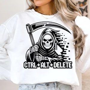 Puede incluir: Sudadera blanca con un gráfico en blanco y negro de la Parca sosteniendo una guadaña. El texto "CTRL+ALT+DELETE" está impreso debajo en una fuente en negrita. El diseño es una versión humorística de los comandos informáticos.