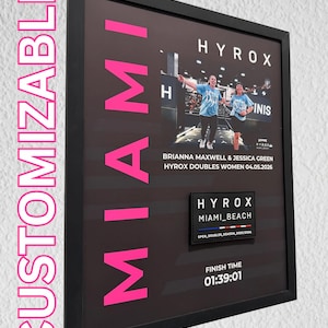 May include: Framed print with the word "MIAMI" in bright pink letters. The print features two women in athletic wear, the text "HYROX DOUBLES WOMEN 04.05.2026", and a finish time of 01:39:01. The word "CUSTOMIZABLE" is on the left side.