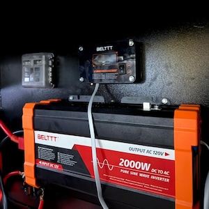 Può includere: Un inverter a onda sinusoidale pura da CC a CA BELTTT nero e arancione da 2000W con un cavo bianco, montato su una superficie scura. Sopra c'è un pannello di controllo nero e una piccola scatola di plastica trasparente. L'inverter ha la scritta "OUTPUT AC 120V".