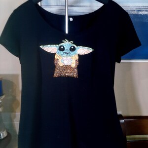 May include: Black short-sleeve t-shirt featuring a rhinestone design of a cartoon character. The design includes light blue, tan, and brown colors. The shirt is hanging on a wooden hanger.