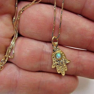 May include: A gold chain necklace with a hamsa hand pendant featuring an iridescent opal stone.