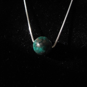 May include: A silver chain necklace with a single, round, dark green gemstone pendant.