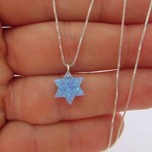 Puede incluir: Un collar de cadena de plata con un colgante de Estrella de David de ópalo azul.