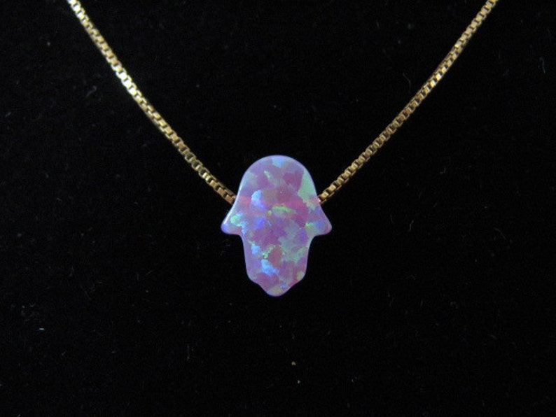 Op de afbeelding: Een gouden ketting met een hanger in de vorm van een hamsa-hand van paarse opaal.