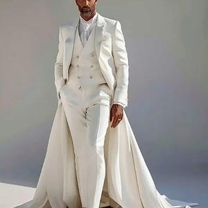 Puede incluir: Un traje blanco formal con una larga cola. El traje incluye un chaleco cruzado, una chaqueta y pantalones a medida. El conjunto se completa con botas blancas. El traje lo lleva una persona con barba.