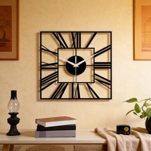 Puede incluir: Reloj de pared cuadrado negro con números romanos y manecillas blancas. El reloj tiene un centro negro y un borde transparente. El reloj está montado en una pared de color amarillo claro. Objetos decorativos sobre una mesa blanca.