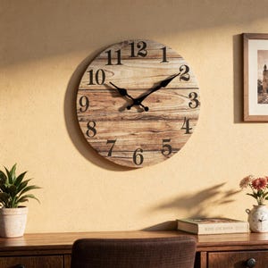 Puede incluir: Reloj de pared redondo con esfera de imitación madera y números negros. Las manecillas del reloj son negras. El reloj está montado en una pared de color amarillo claro. Es un objeto decorativo.
