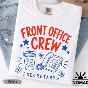 May include: A white t-shirt featuring the red text FRONT OFFICE CREW and blue text SECRETARY. The graphic includes a blue line-art illustration of a drink cup with ice and a landline telephone, accented by blue stars and small flower icons.