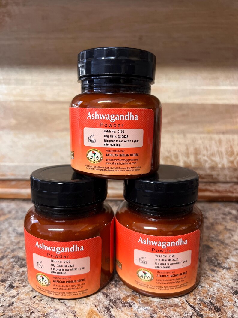 May include: Three small glass jars of Ashwagandha powder are stacked. Each jar has a black lid and a red label with white text. The labels include the text "Ashwagandha Powder", batch and manufacturing information, and the manufacturer's name.