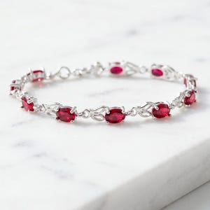Peut inclure: Un bracelet de couleur argentée orné d'une série de pierres précieuses rouge foncé de taille ovale. Les pierres sont serties dans des maillons métalliques complexes et entrelacés qui relient chaque gemme, formant une chaîne continue.