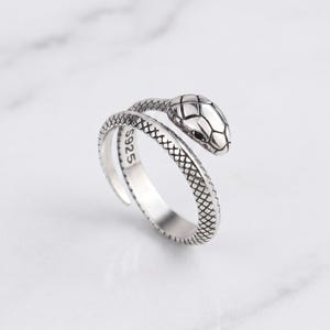 Peut inclure: Une bague ouverte en argent en forme de serpent enroulé avec des détails d'écailles texturées sur l'anneau et la tête. La surface intérieure de la bague porte l'inscription S925, indiquant la composition métallique de ce bijou.