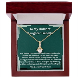 May include: A gold-tone pendant necklace with a central round cubic zirconia stone, presented in a dark wood box. The box insert features the text: To My Brilliant Daughter Isabella, Your dedication to merging medicine and engineering inspires me every day. With Eternal Pride Michael.