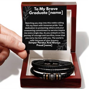 May include: A black braided leather bracelet with silver and gold accents, presented in a wooden gift box. The box contains a card with the text "To My Brave Graduate" and a heartfelt message. The bracelet is inscribed with "love you forever".