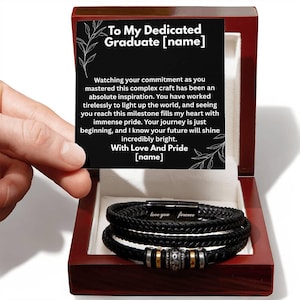 May include: A black braided leather bracelet with silver and gold accents, presented in a wooden gift box. The box contains a card with the text "To My Dedicated Graduate" and a heartfelt message. The bracelet is engraved with "love you forever".
