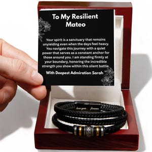 May include: A black braided leather bracelet with a metal clasp engraved with the words love you forever, featuring silver and gold-toned beads, presented in a dark wood box with a card reading To My Resilient Mateo and a message of support.