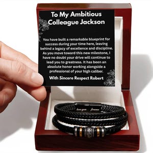 May include: A black braided leather bracelet with metallic beads and a magnetic clasp engraved with "love you forever," presented in a dark wood box with a message card addressed to "Ambitious Colleague Jackson" from "Robert."