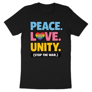 Può includere: T-shirt nera con le parole "PEACE. LOVE. UNITY." in blu, rosa e giallo. Un cuore con un simbolo di pace nei colori dell'arcobaleno è tra "LOVE" e "UNITY". Il testo "(STOP THE WAR.)" è sotto.