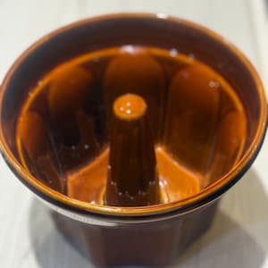 May include: A brown ceramic bundt pan with a central tube and a fluted design. The pan has a glossy finish and a rich, warm color, perfect for baking cakes and other treats.
