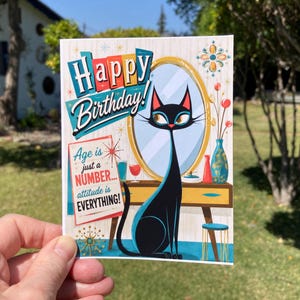 May include: A rectangular greeting card featuring a black cat sitting in front of a vanity mirror. The text reads Happy Birthday! Age is just a NUMBER... attitude is EVERYTHING! The illustration includes a blue vase, a red glass, and a stool.