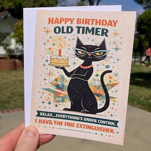 May include: A birthday card featuring the text "HAPPY BIRTHDAY OLD TIMER" and a black cat illustration wearing glasses and a pearl necklace. The cat holds a cake with a lit candle. The card also reads "RELAX...EVERYTHING'S UNDER CONTROL. I HAVE THE FIRE EXTINGUISHER."