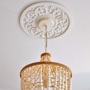 May include: A white beaded chandelier with a brown jute rope trim and a tassel. The chandelier is hanging from a white ceiling medallion with a decorative design.