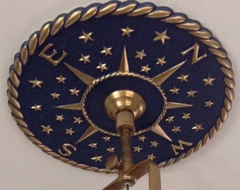 May include: A gold ceiling fixture with a blue and gold compass design. The compass features a gold star design and the letters N, S, E, and W.
